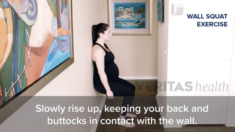 A woman performing wall squat exercise.