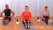 Two women and a man sitting on yoga mats in an exercise studio
