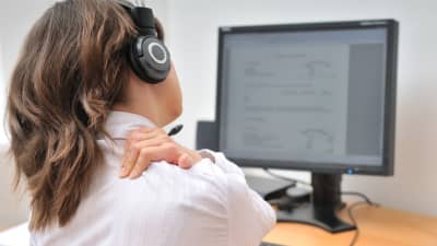 Woman working at a computer, grabbing her neck in pain