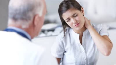 Woman grabbing her neck in pain while talking with a doctor