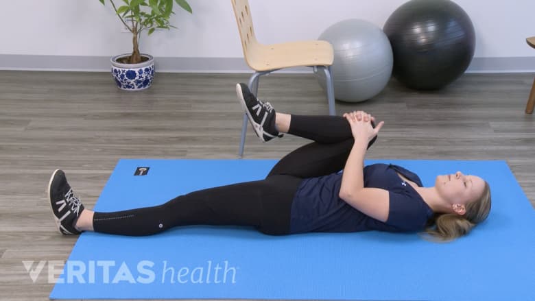 Woman performing a single leg, knee-to-chest stretch on a yoga mat.