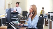 Young professional women taking a phone call at her desk in a busy office.