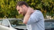Man holding his neck and his damaged car in the background