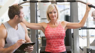 Woman doing arm exercises with a trainer in a gym.