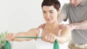 Woman working with physical therapist stretching a resistance band with both hands outstretched