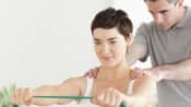 Woman working with physical therapist stretching a resistance band with both hands outstretched