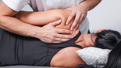 Posterior view of a masseuse massaging a woman's upper shoulder.