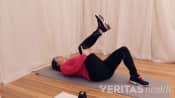 Woman lying on yoga mat doing single knee to chest stretch.