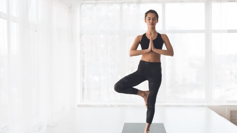 Woman performing tree pose yoga stretch on a yoga mat.