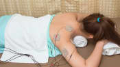 Woman lying prone with a TENS unit connected to the upper back.