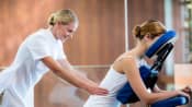 Masseuse working on the lower back of a person in a massage chair.