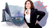 Woman grabbing her lower back while sitting at her desk.