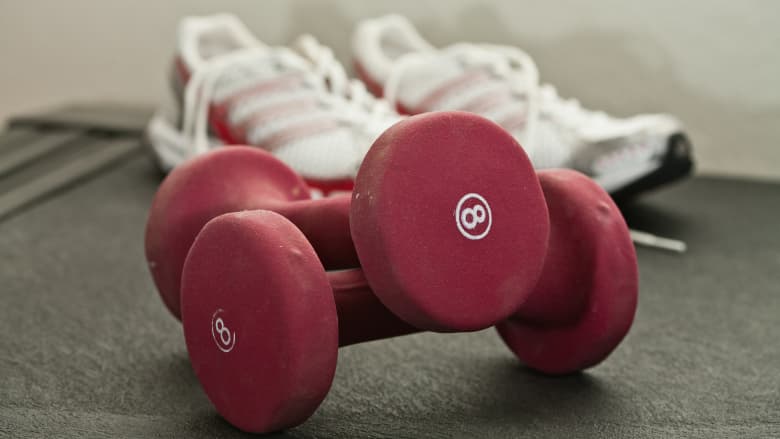Two dumbbell weights and a pair of athletic shoes on the ground.