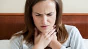 Woman in a bed holding her throat in pain