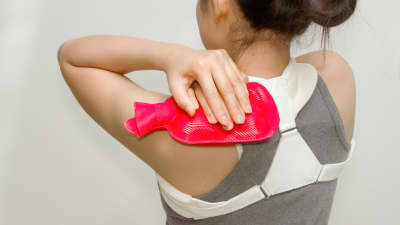 Woman applying a hot pack to her upper back