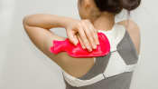 Woman applying a hot pack to her upper back