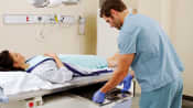 Patient lying on X-ray table while X-ray technician switches out the X-ray films beneath her.