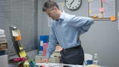 Man standing at his desk, grabbing his lower back in pain