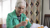 Woman sitting at a table reading the label on a prescription bottle