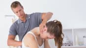 Male physical therapist examining a young woman's cervical and thoracic spine in the medical office