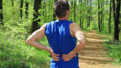 Man grasping lower back on running trail