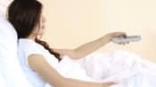 Woman resting in bed holding a television remote