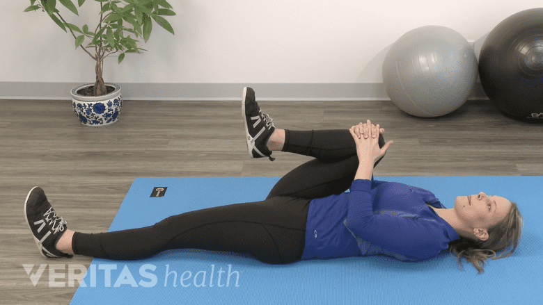 Una fisioterapeuta demostrando el estiramiento de rodilla al pecho.