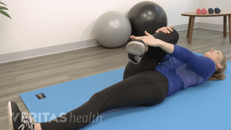 Woman performing supine piriformis stretch on a yoga mat.