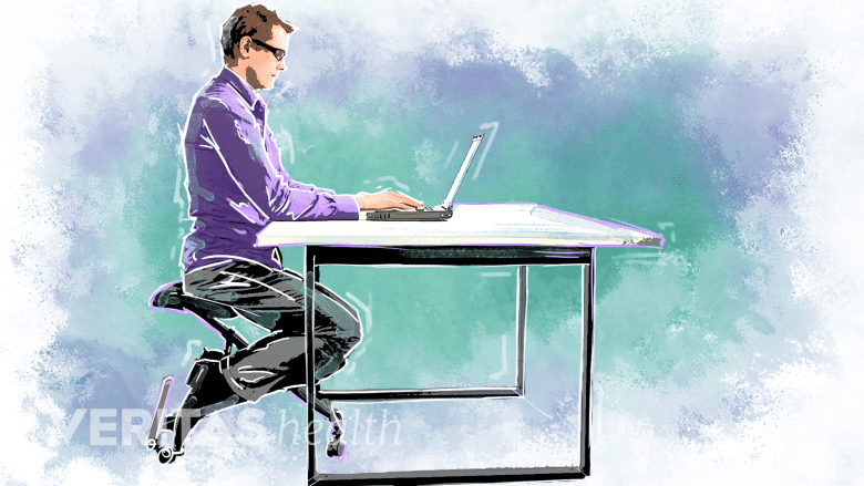 Man sitting at a kneeling chair at a desk.